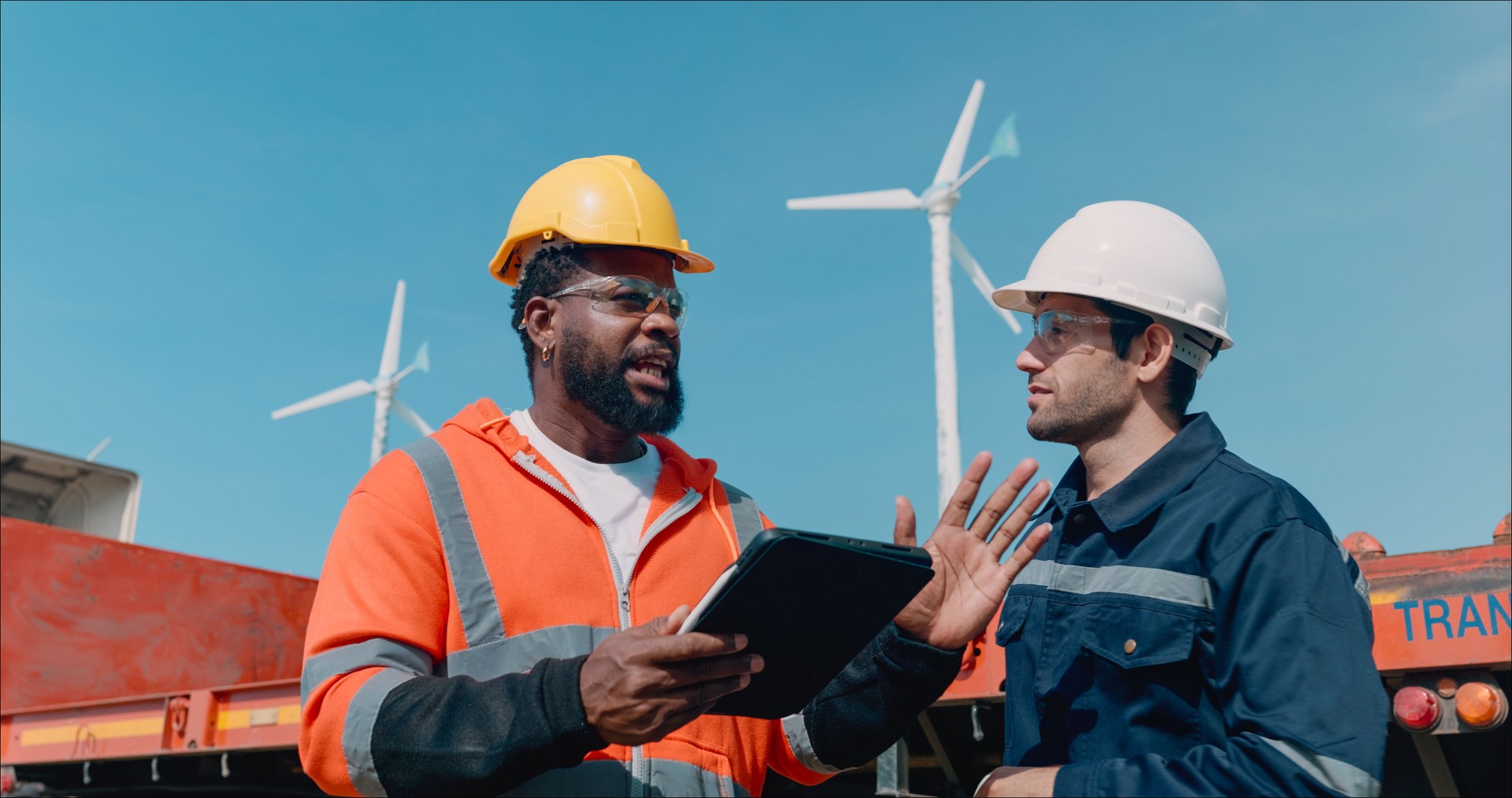 Two Professional Male Managers Wearing Hard Hats Check Inventory and Orders Delivering goods via Airfreight, Seafreight, and inland transit to customers via an application on a digital tablet, employees work in a distribution center in the logistics busin